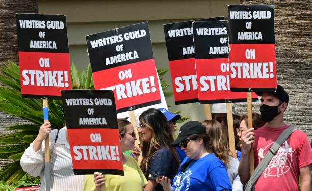 Writers hold signs while picketing in front of Paramount Studios in Los Angeles, California on May 15, 2023 as the strike by the Writers Guild of America enters its third week. The thousands of picketing writers say they are striking for better compensation in a field that has been disrupted by the streaming industry. Writers say they are looking for more stable working conditions and a better share of the profits generated by the rise of streaming. (Photo by Frederic J. BROWN / AFP) (Photo by FREDERIC J. BROWN/AFP via Getty Images)