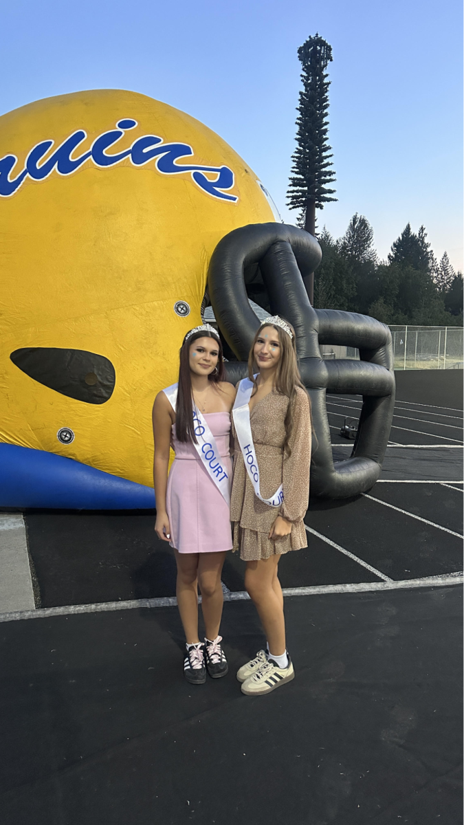 Caption: Seniors Leila Mokan and Yanna Ovcharenko pose next to the Barlow Bruin Helmet before walking out during half time of a football game for homecoming court

